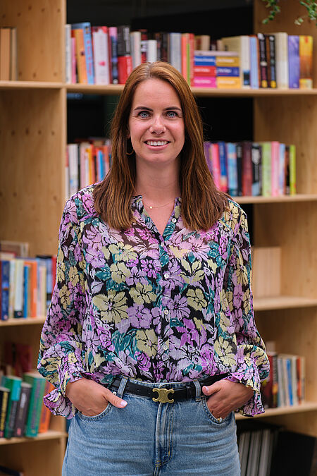 portret van een lachende vrouw met rode haren en kleurvolle blouse.