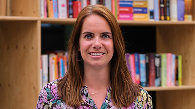 portret van een lachende vrouw met rode haren en kleurvolle blouse.