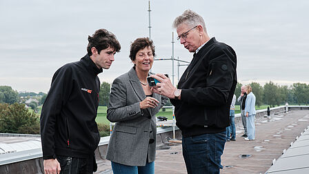 Interactie tussen drie personen op het dak met smartphone.