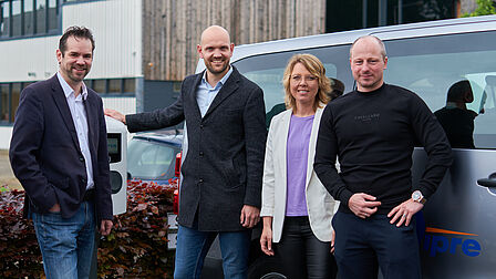 Groep van vier mannen en een vrouw poseren trots naast een elektrische lader.