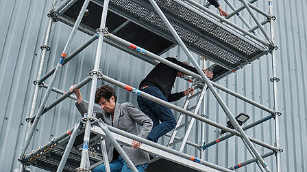 Een aantal mensen dalen af via een hoge stellage naast het gebouw.
