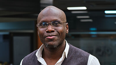 poserende man in een net grijs hesje, wit shirt en een spijkerbroek.