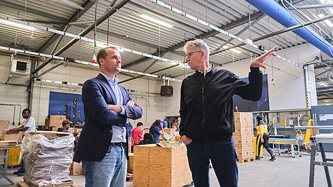 Twee mensen staan in een grote productiehal.
