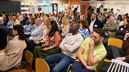 Grote groep mensen aan het luisteren naar een presentatie.