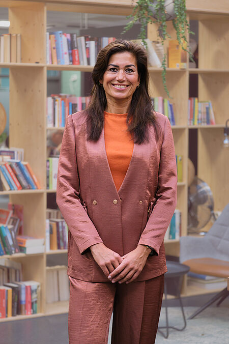 portret van een vrouw met lange donkere haren en zalmkleurig pak.