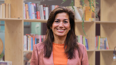 portret van een vrouw met lange donkere haren en zalmkleurig pak.