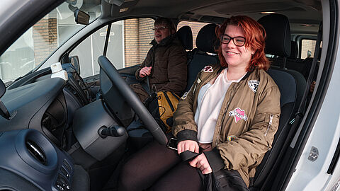Jonge vrouw met rode haren zit achter het stuur van een busje.