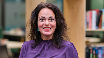 vrouw in paarse blouse poseert voor een boekenkast