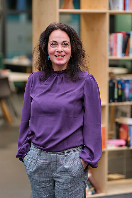 vrouw in paarse blouse poseert voor een boekenkast