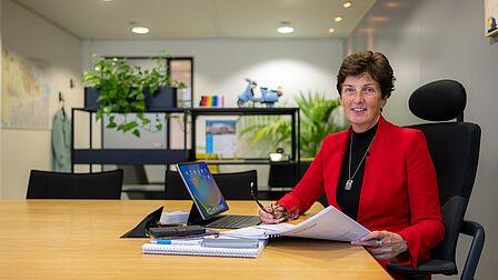 Portret van een vrouw met documenten en een computer in een kantoorruimte.