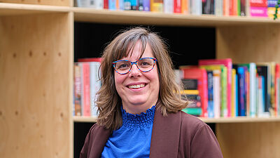 vrouw met bril poseert voor een boekenkast