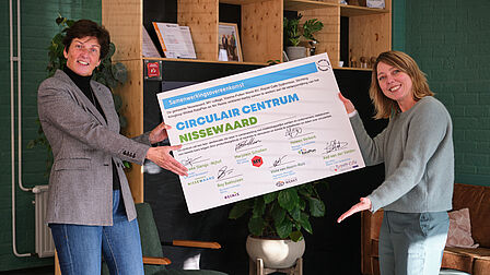 Twee mensen presenteren een groot certificaat met ondertekening.