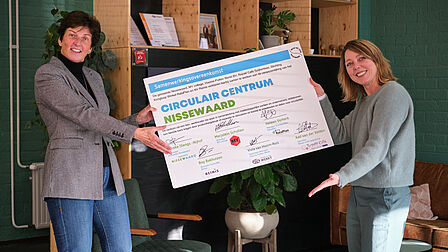 Twee mensen presenteren een groot certificaat met ondertekening.