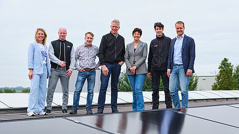 Groep mensen poseren achter reflecterende zonnepanelen.