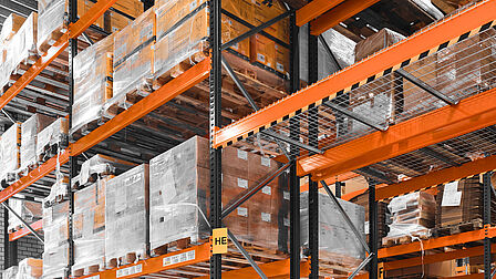 Grote hal met stellages en hoog gestapelde pallets met dozen.