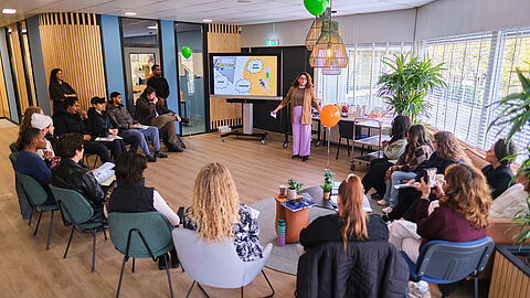 Grote groep mensen in een kring van stoelen tijdens de presentatie.