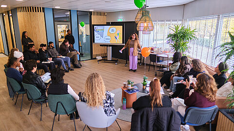 Grote groep mensen in een kring van stoelen tijdens de presentatie.
