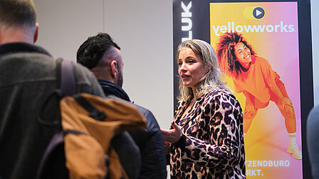 Een vrouw en meerdere personen voor een banner.