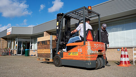 Achteruit rijdende heftruck met pilonnen en een instructeur.