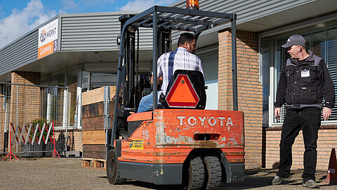 Achteruit rijdende heftruck met pilonnen en een instructeur.